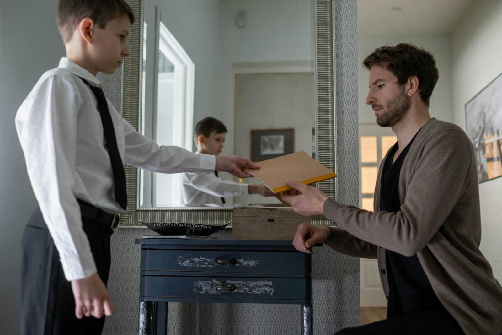 A father and son exchanging an envelope in an indoor setting, reflecting parenthood and communication.